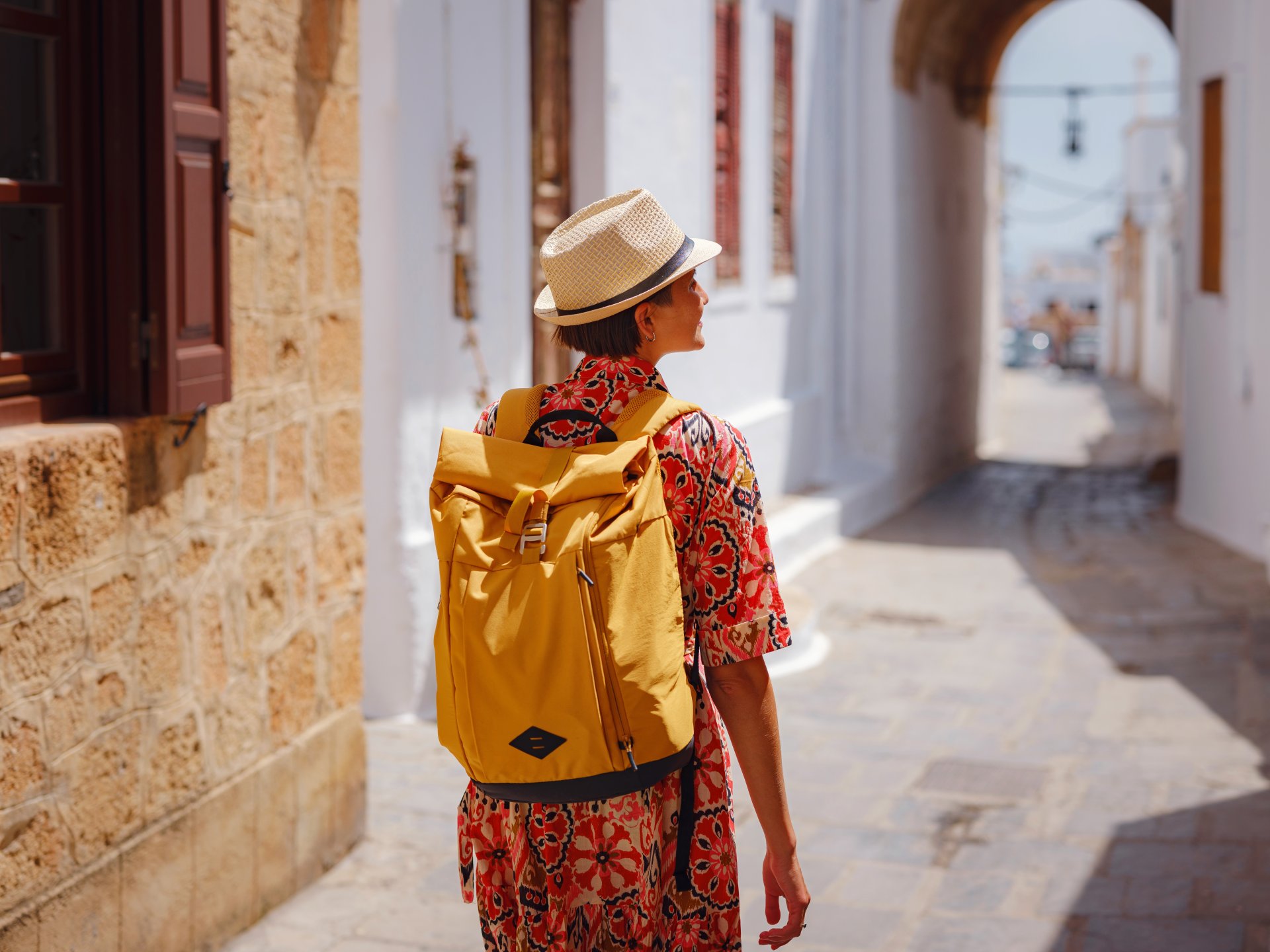 femeie imbracata lejer in stil boho merge pe strazile inguste din Lindos in Grecia intr-o zi insorita de vara atmosfera de vacanta relaxare si explorare pe insula mediteraneana