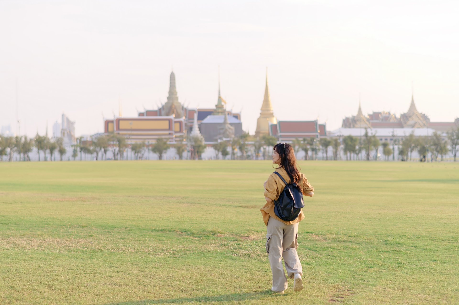 femeie calatoreste la wat pra kaew cu rucsac pe umar soarele straluceste pe acoperisurile aurii si zambetul ei este fara griji