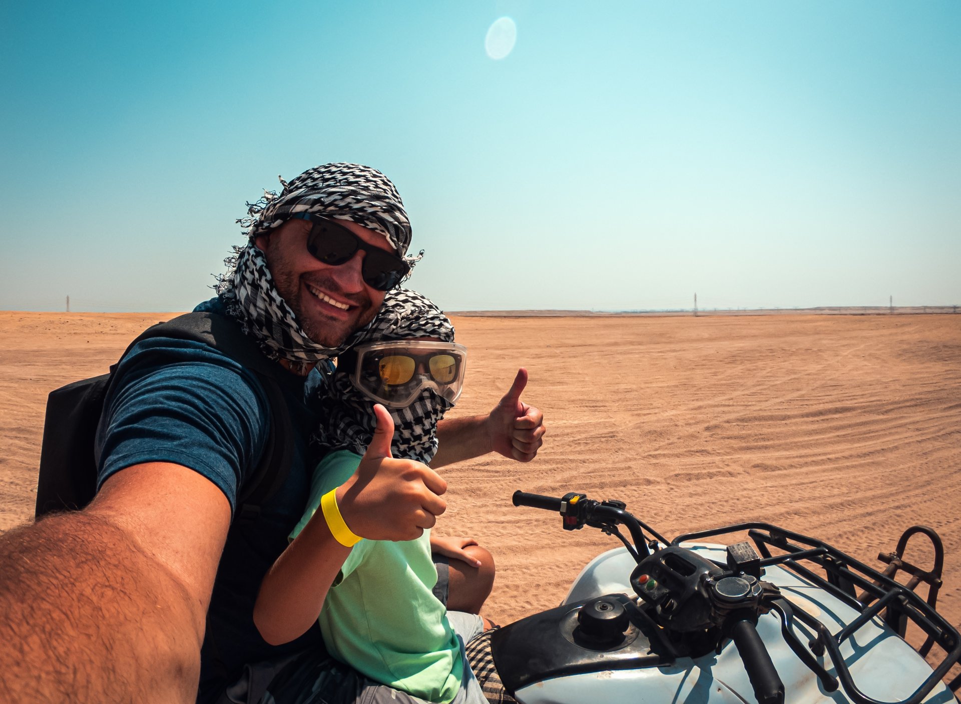 tata si fiu fac selfie in timp ce conduc un quad in desert si baiatul arata semnul thumbs up spre camera