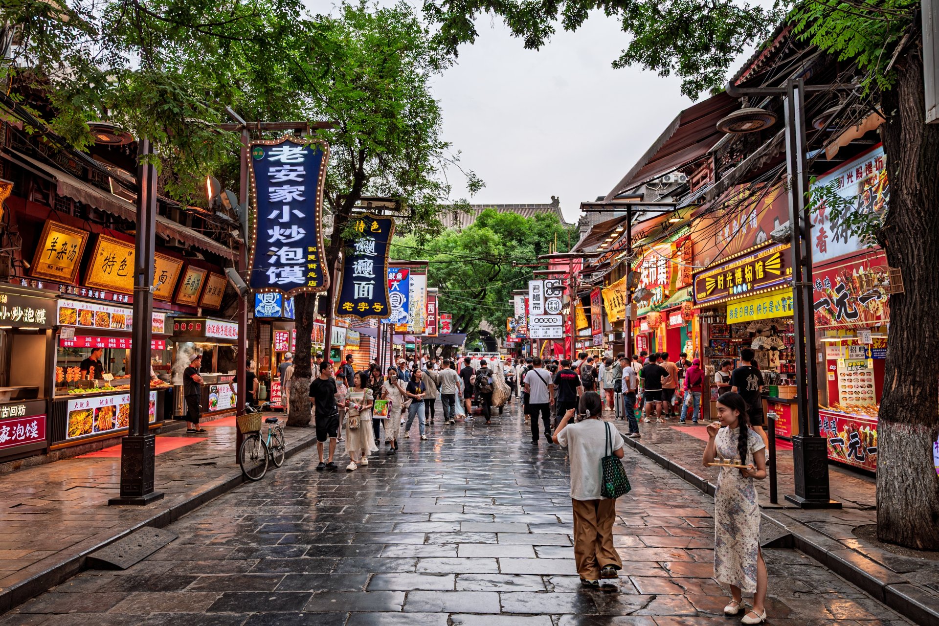Strada animata din cartierul Xi'an, unde localnici si turisti se plimba printre magazine traditionale, tarabe cu mancare si cladiri cu arhitectura specifica zonei istorice.