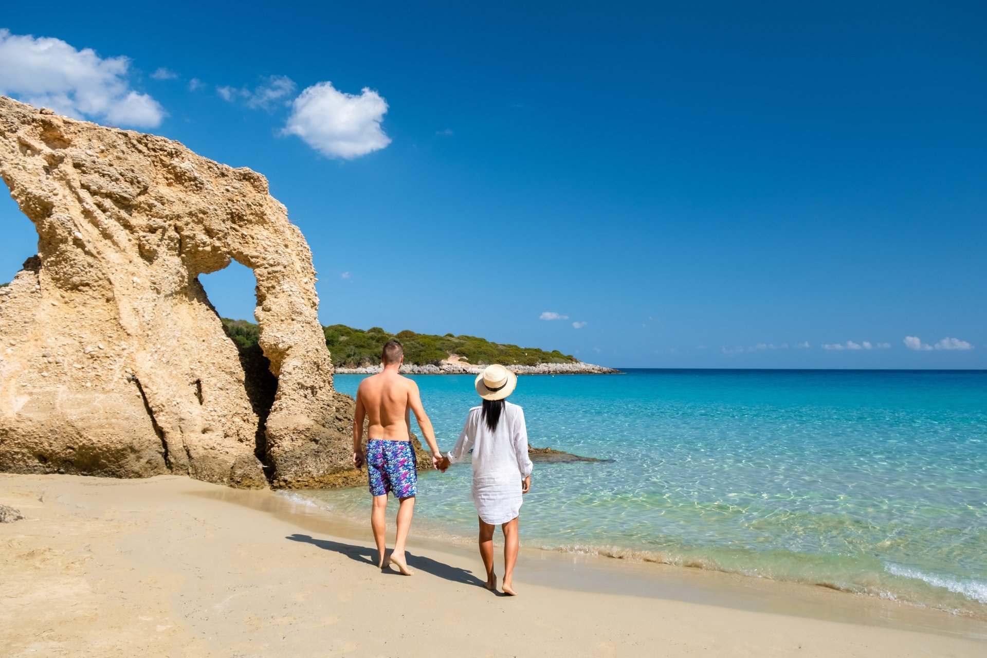 un cuplu tanar relaxandu-se pe plaja Voulisma din zona Istron, Creta, cu apa turcoaz si nisip auriu, intr-o zi insorita de vara in Grecia