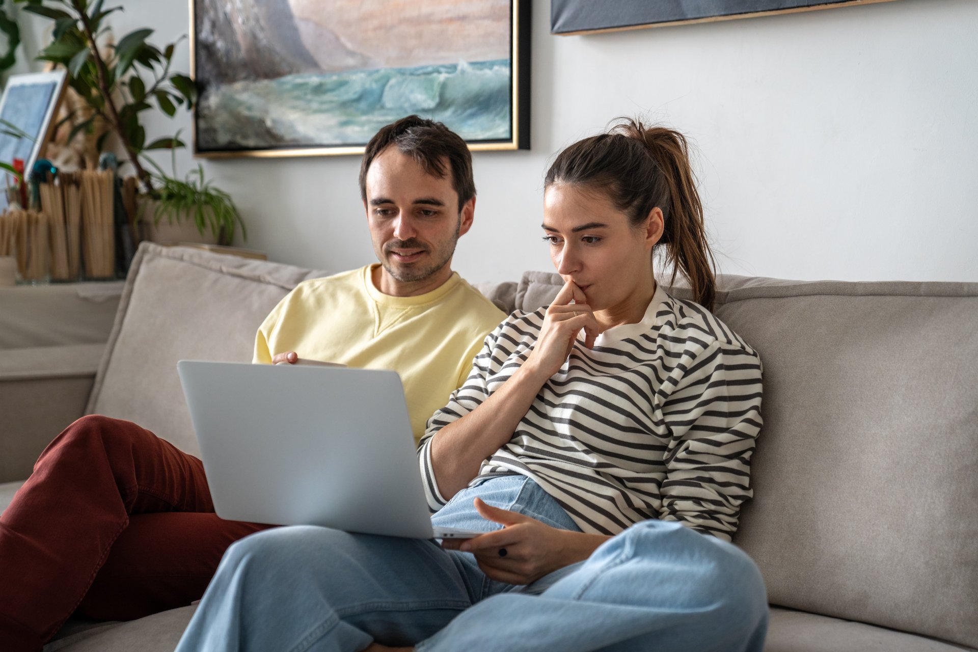 Cuplu aflat acasa analizeaza pe laptop mai multe optiuni de cazare, compara preturi si planifica urmatoarea vacanta, intr-o atmosfera relaxata si colaborativa