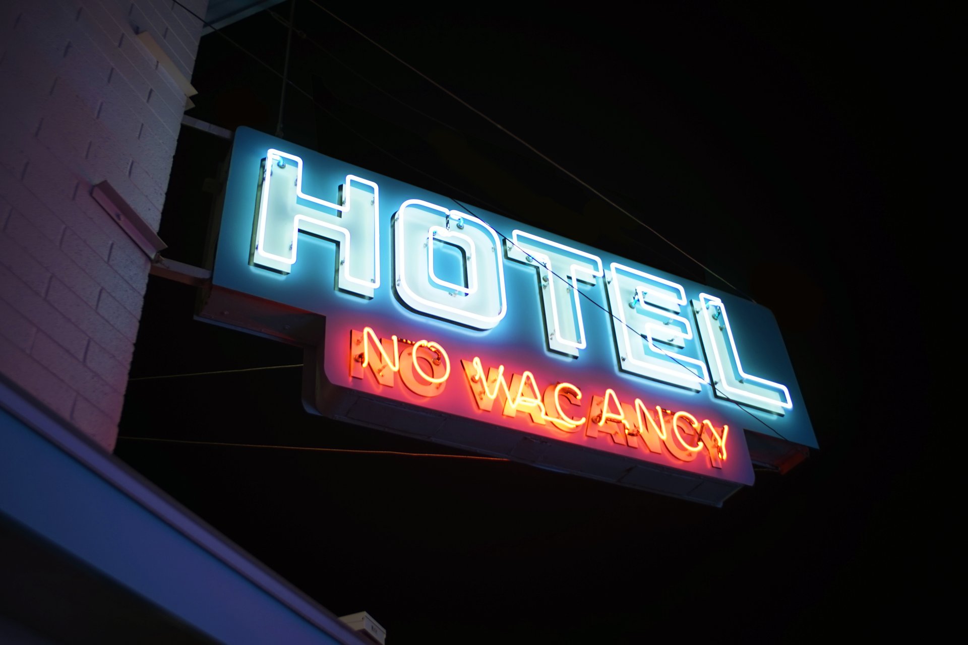 Indicator luminos cu mesajul "No Vacancy" amplasat pe fatada unui hotel sau motel intr-o zona centrala a orasului, sugerand ca nu mai sunt camere disponibile.