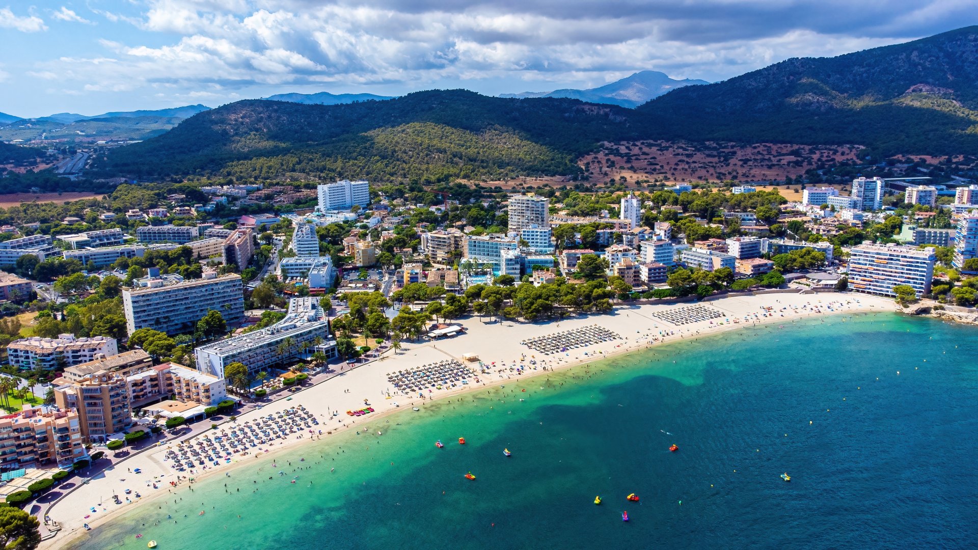 Vedere aeriana asupra plajei Es Carregador din Palmanova, cu apa turcoaz, nisip fin, sezlonguri si statiunea de la malul Marii Mediterane din insula Mallorca, Spania.
