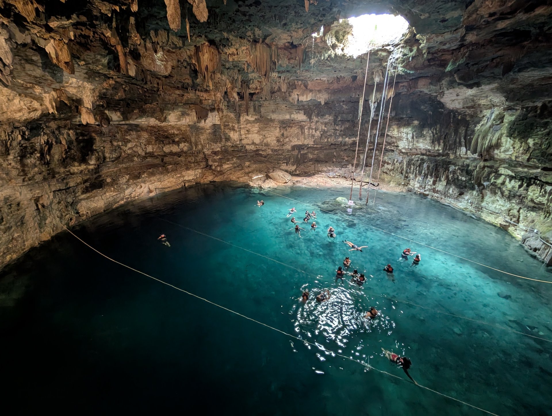 Turiști înotând în apele din Cenote Samula, parte a Cenote Xkeken, în apropiere de Valladolid, cu formațiuni stâncoase spectaculoase și lumină naturală filtrată prin deschiderea cenotei
