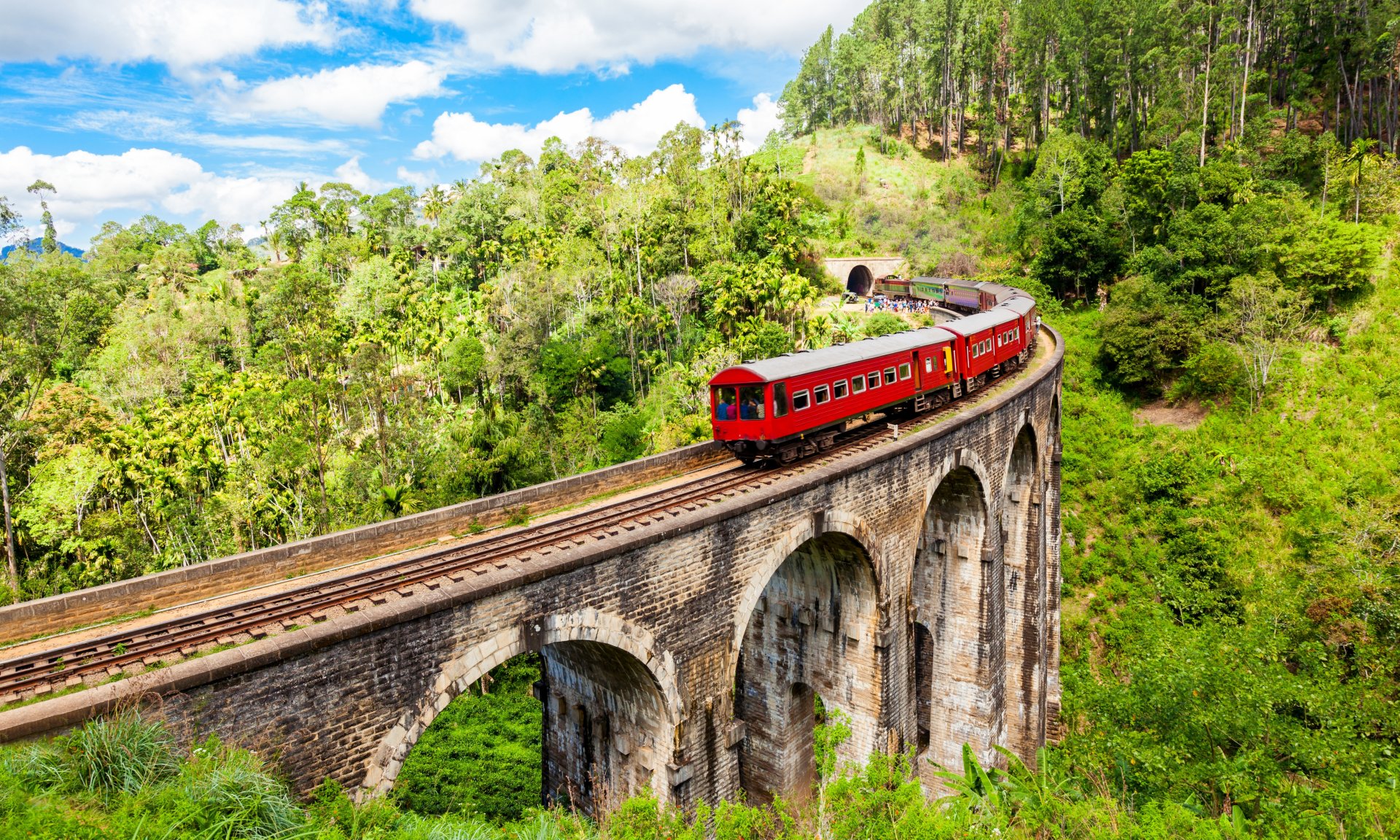 podul iconic cu noua arcade din Sri Lanka, inconjurat de vegetatie tropicala si plantatii de ceai, cu un tren trecand pe viaduct intr-un peisaj montan verde si ceata usoara