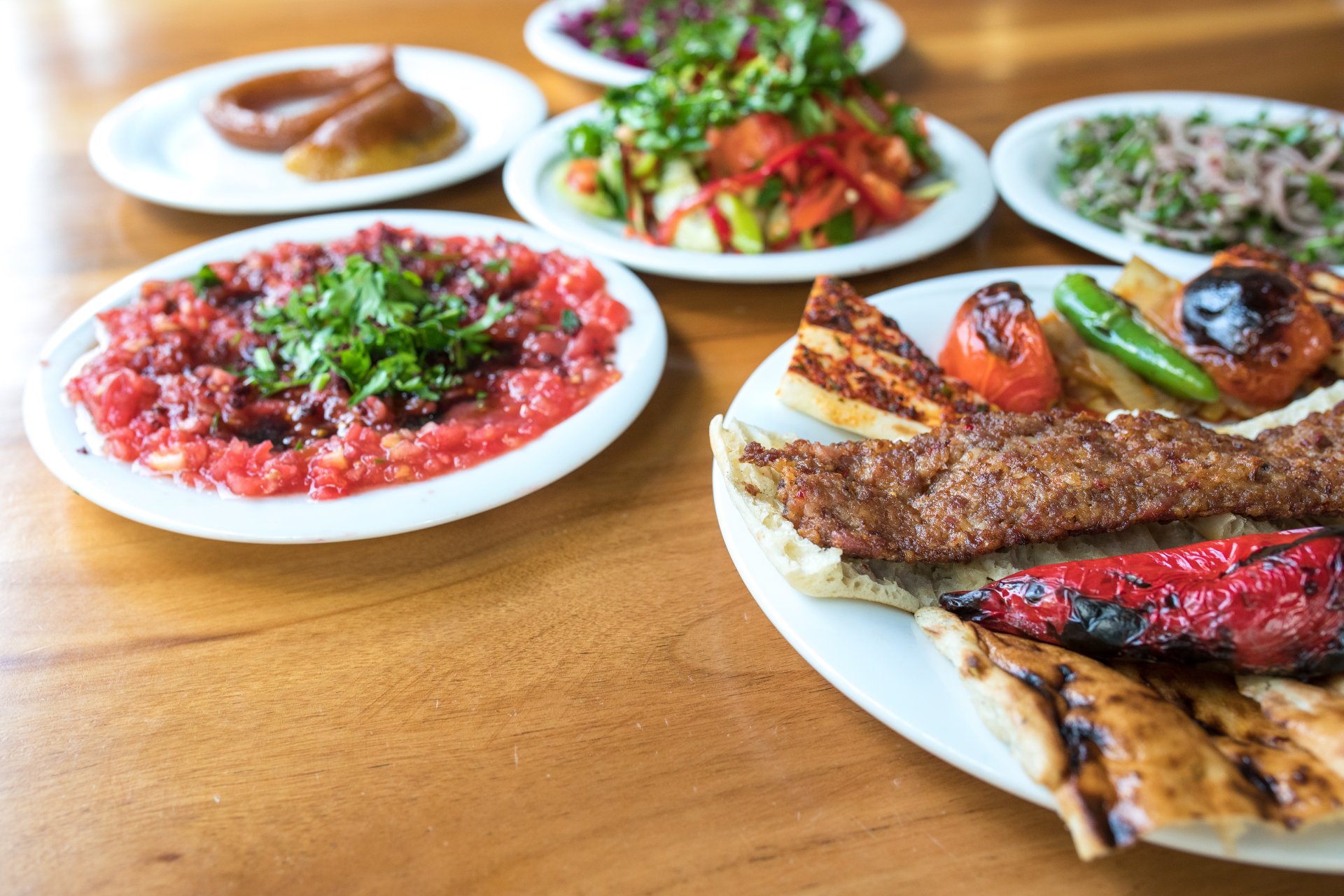 O masa intr-un restaurant turcesc cu Adana kebab servit alaturi de salate proaspete, lipie si aperitive meze, intr-o atmosfera calda de seara, cu preparate specifice bucatariei traditionale din Turcia