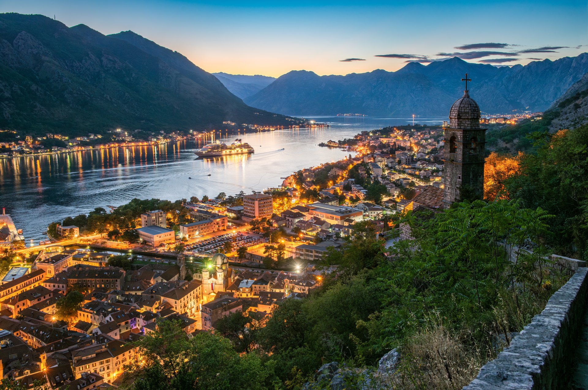 Panorama surprinsa la apus asupra orasului vechi Kotor, cu biserica, acoperisurile istorice si Golful Kotor scaldate in lumina calda a serii, pe coasta Adriaticii din Muntenegru.