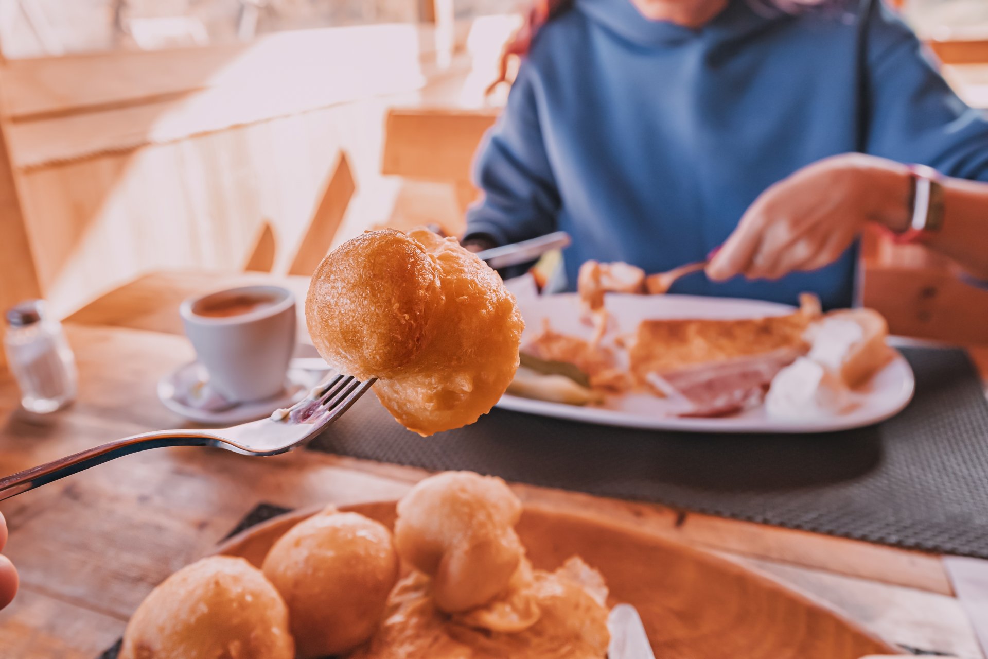 Furculita tine o priganica proaspat prajita, in timp ce o femeie ia micul dejun la un restaurant traditional din Muntenegru, intr-o atmosfera relaxata.
