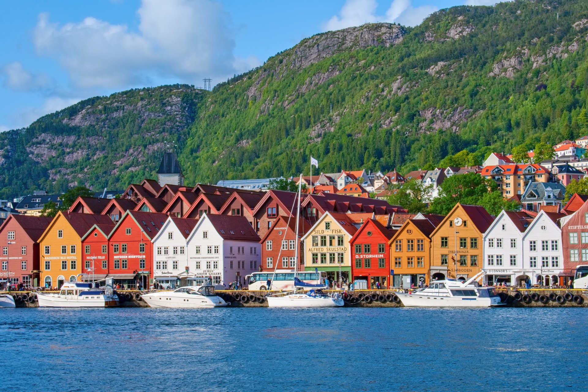 Case traditionale din lemn, vopsite in culori vii, aliniate pe faleza din portul istoric Bryggen din Bergen, cu apa si ambarcatiuni in prim-plan.