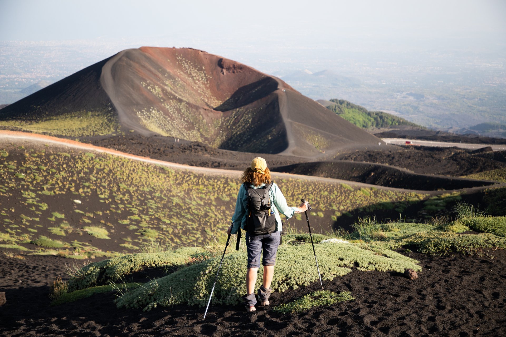 Turist urcand pe traseele vulcanului Etna, inconjurati de peisaje vulcanice si roci formate in urma eruptiilor.