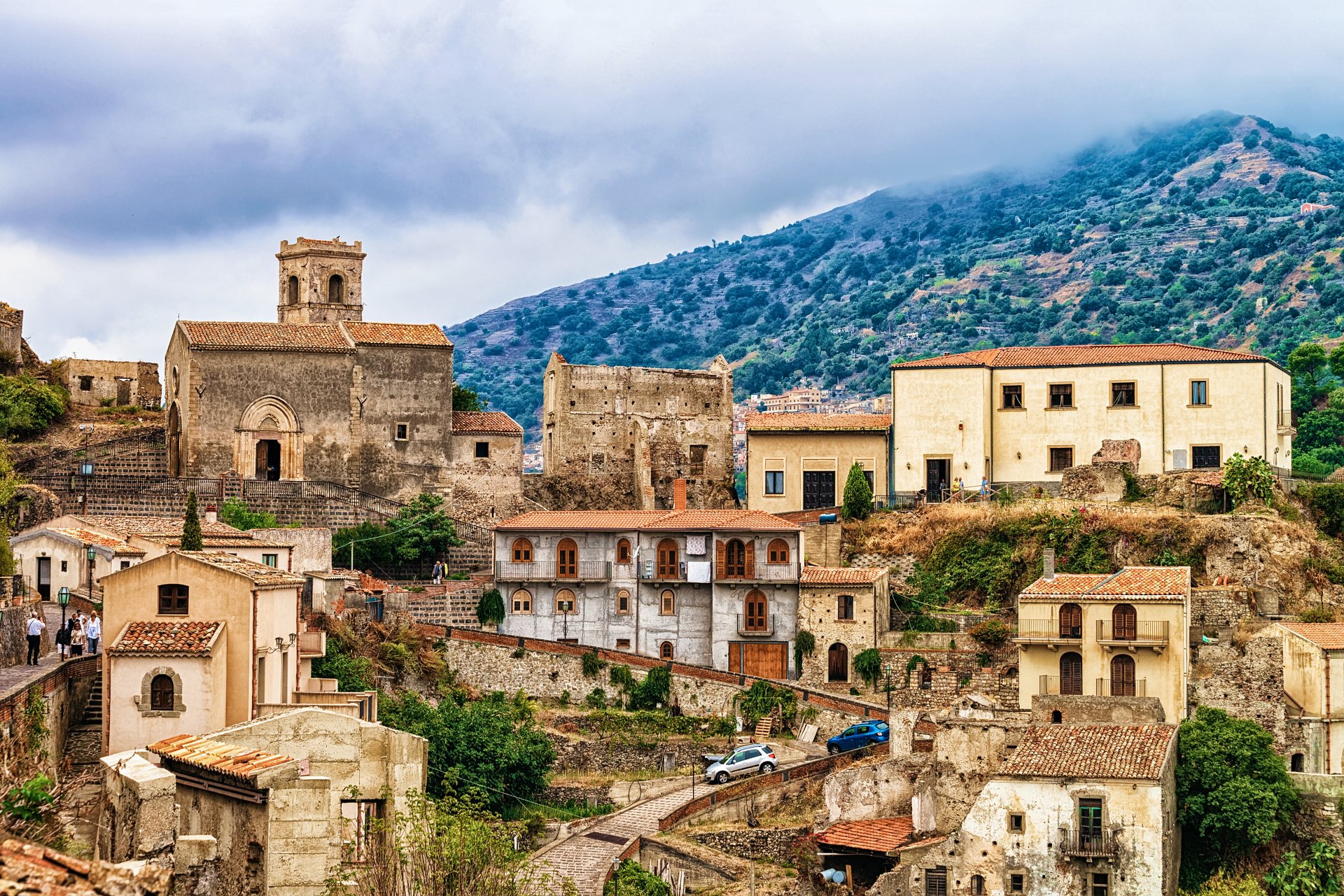 Panorama asupra satului Savoca, asezat pe versantul unui munte din Sicilia, cu case din piatra, stradute inguste si vegetatie mediteraneana in jur.
