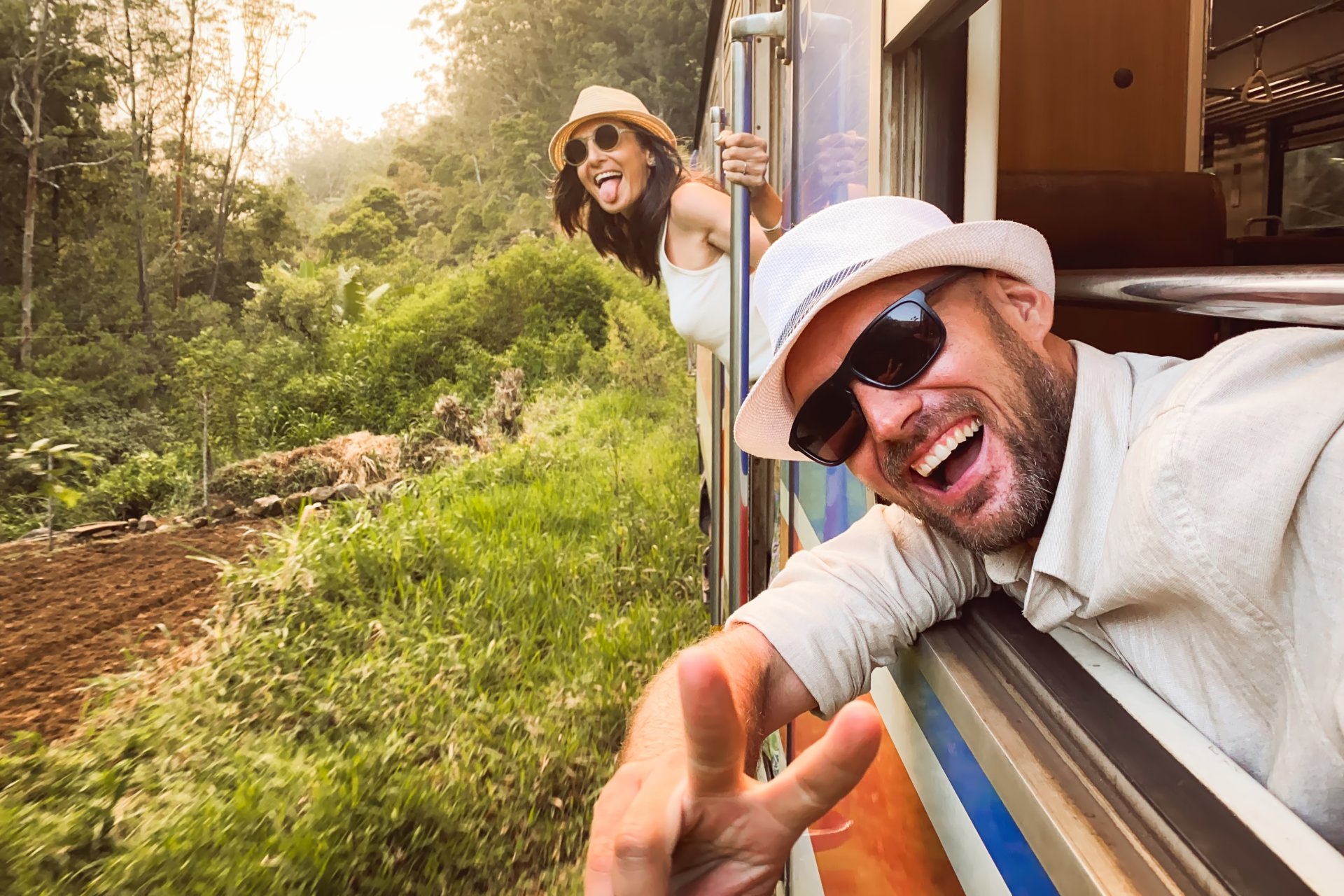 Cuplu de turisti stand in tren in Sri Lanka, admirand peisajele cu plantatii de ceai verzi si dealuri in departare, in timpul unei calatorii relaxante prin zona montana