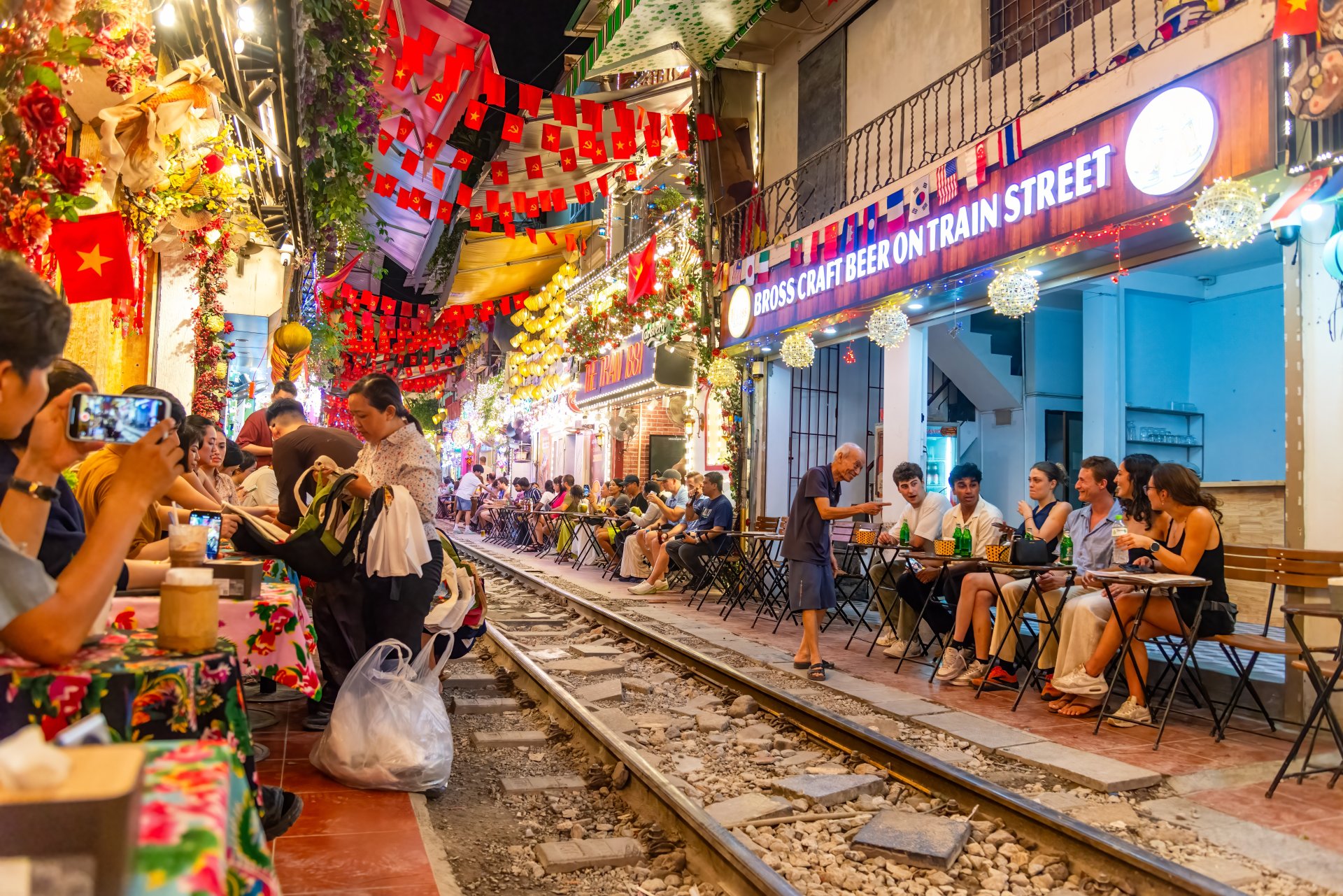 Turisti si localnici se bucura de cafea si bauturi de-a lungul celebrului Train Street din Hanoi, cu lumini colorate si decor festiv.