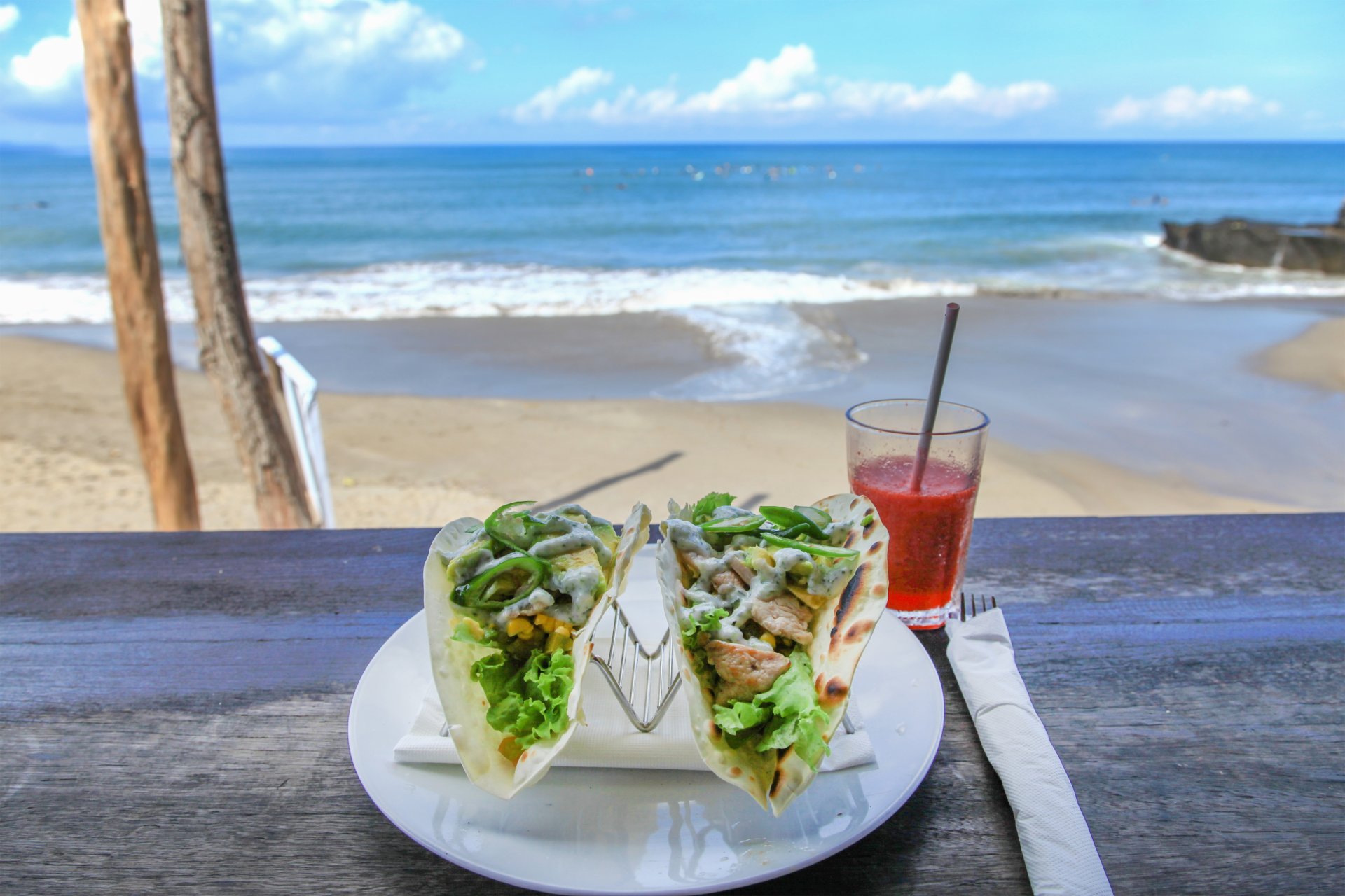 Taco cu pui și avocado, alături de suc proaspăt de căpșuni, savurat la soare pe terasa unui restaurant cu vedere la plajă