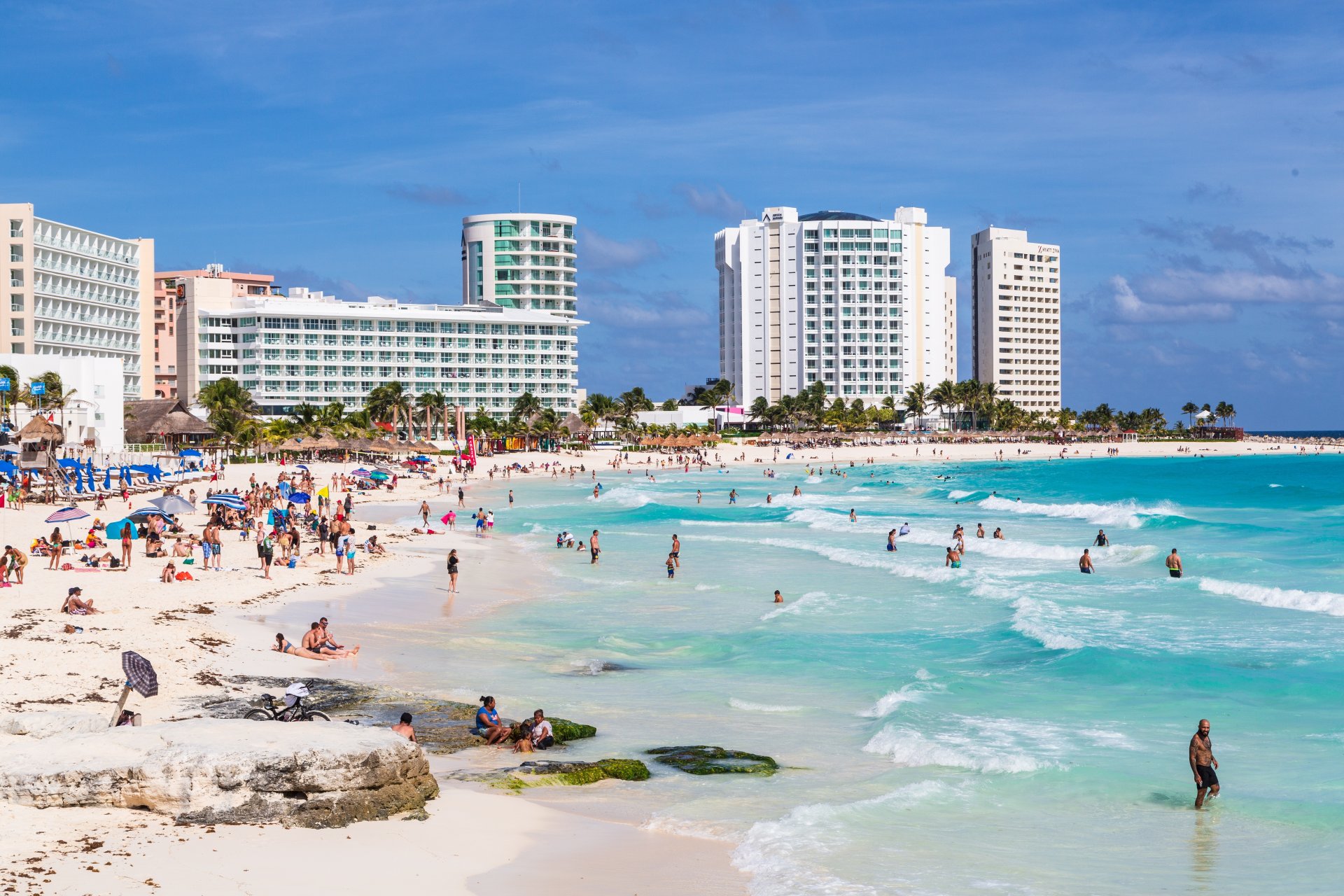 Turisti pe plaja din Cancun, apa turcoaz a Marii Caraibilor, hoteluri si oameni pe tarm si in apa